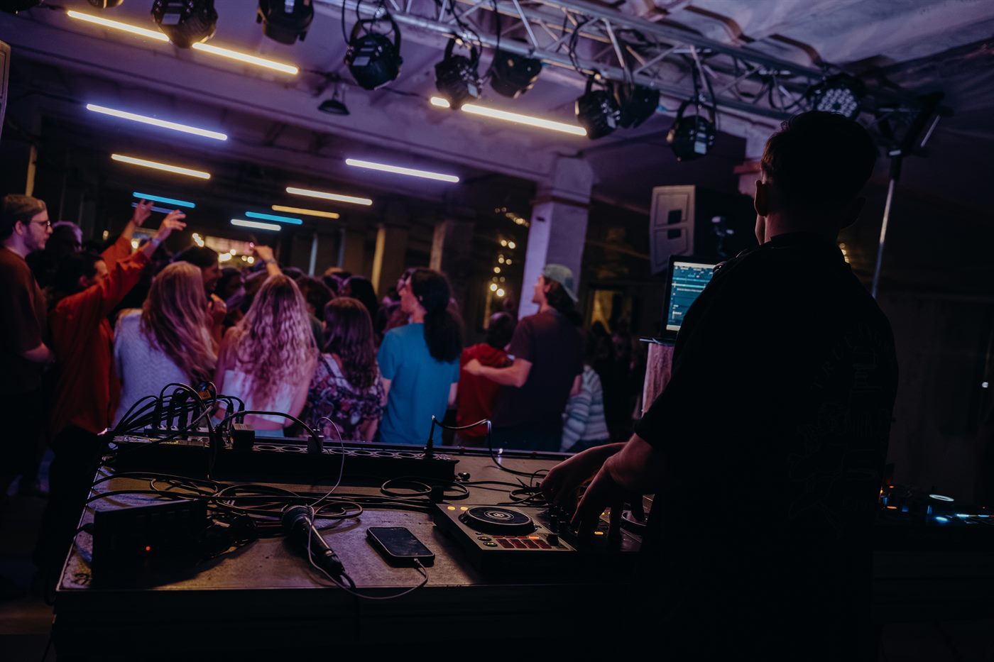 A DJ a pult mögött, előtte a táncoló vendégek, felettük a fénytechnika