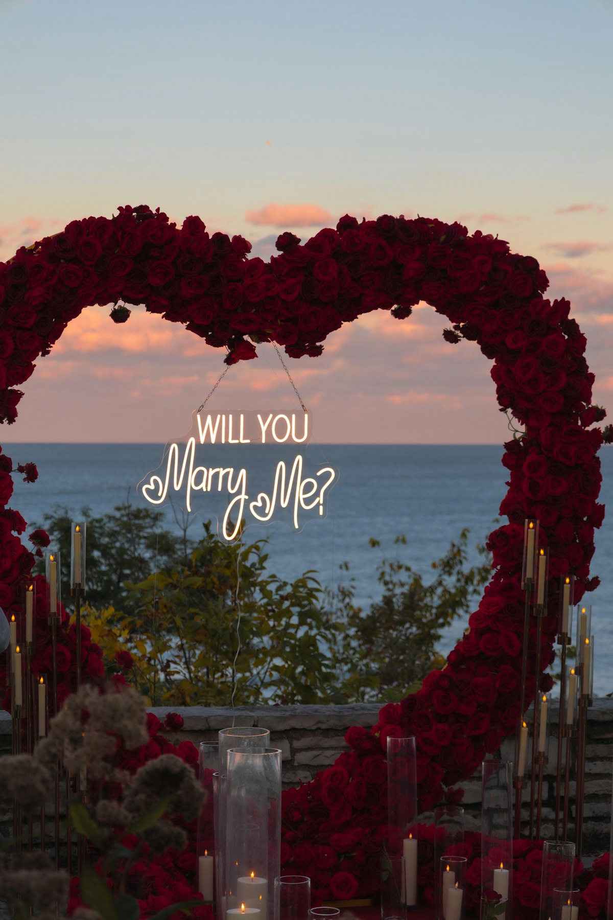 Szív alakú rózsadekoráció, Will You Marry Me felirattal, tengerparti naplementében